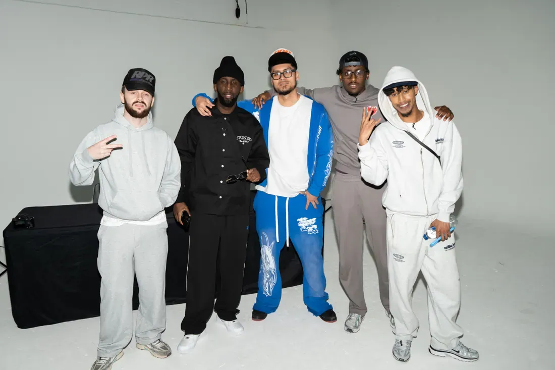 Five contributors in tracksuits lined up on a lit white cyc, mid-take