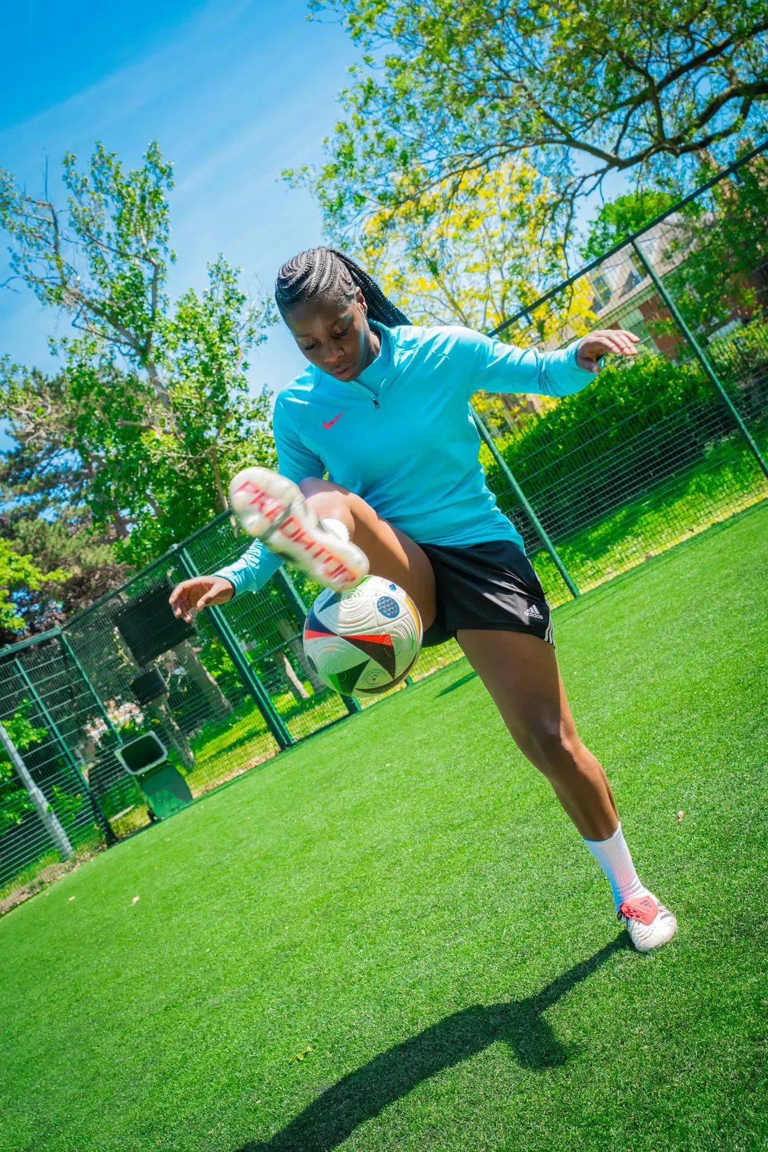 A footballer striking a ball on a sunlit grass pitch